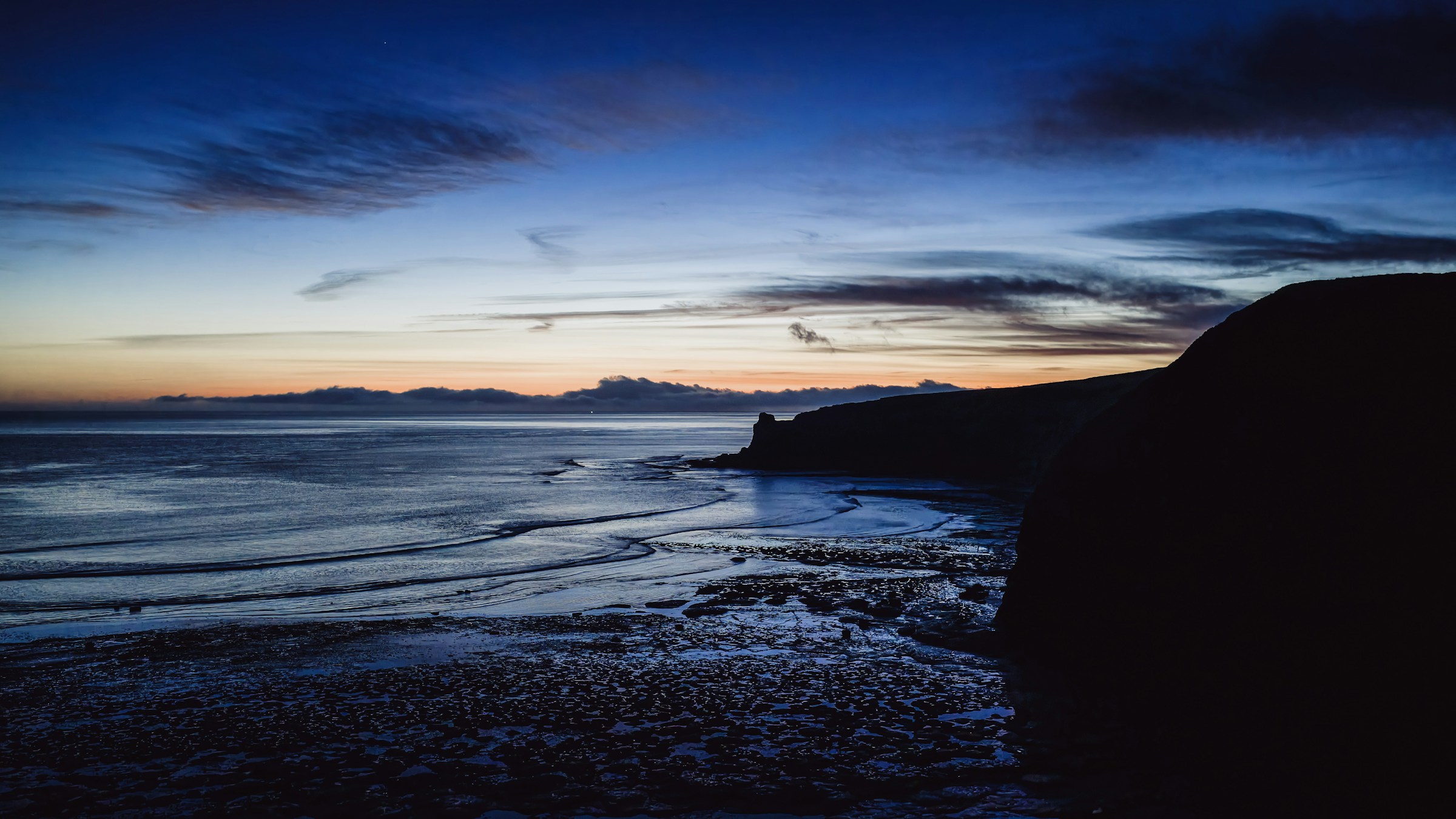Moody dark water and a restrained coastal horizon at dusk.